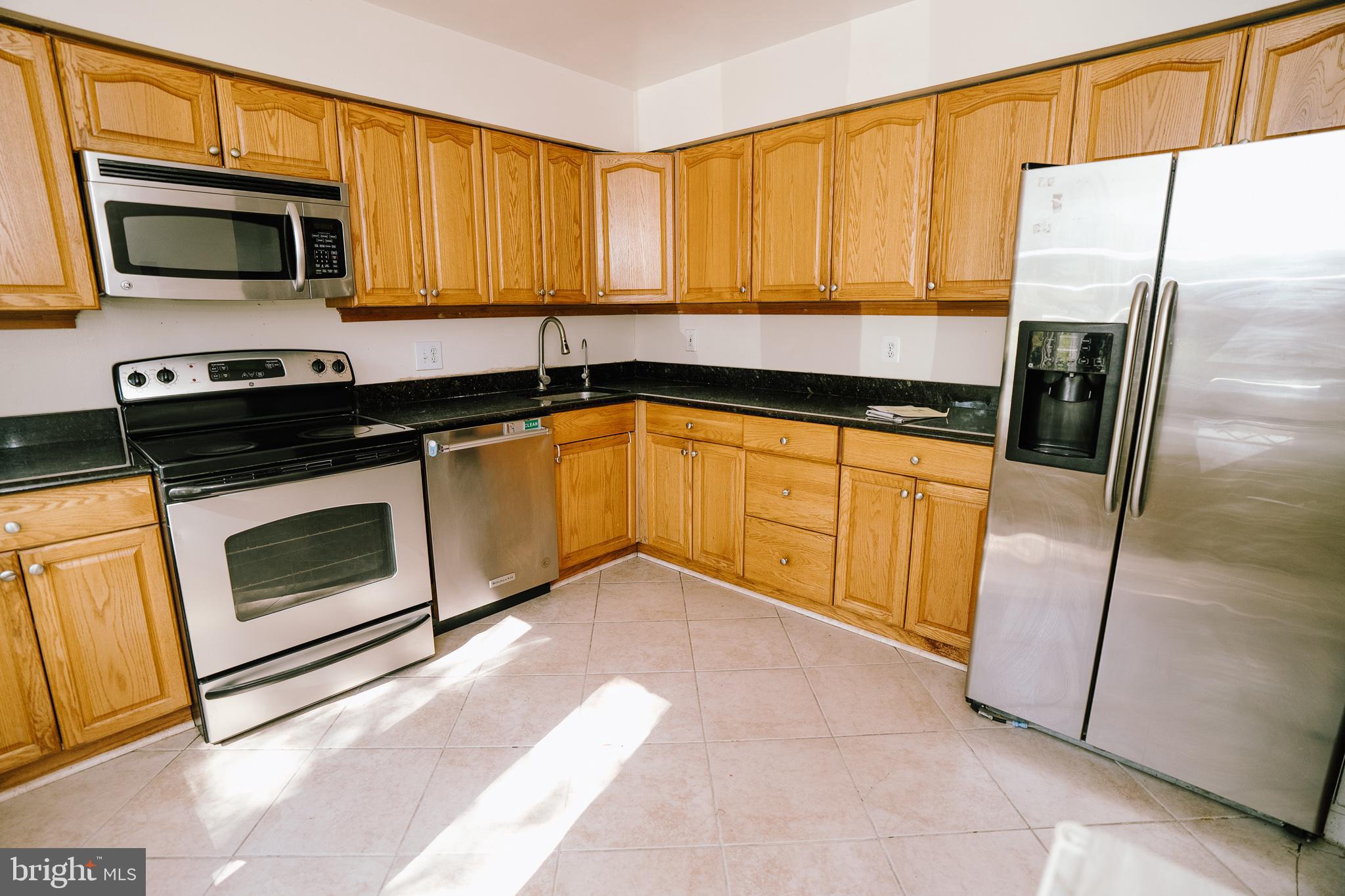 a kitchen with granite countertop a refrigerator a microwave a sink and cabinets