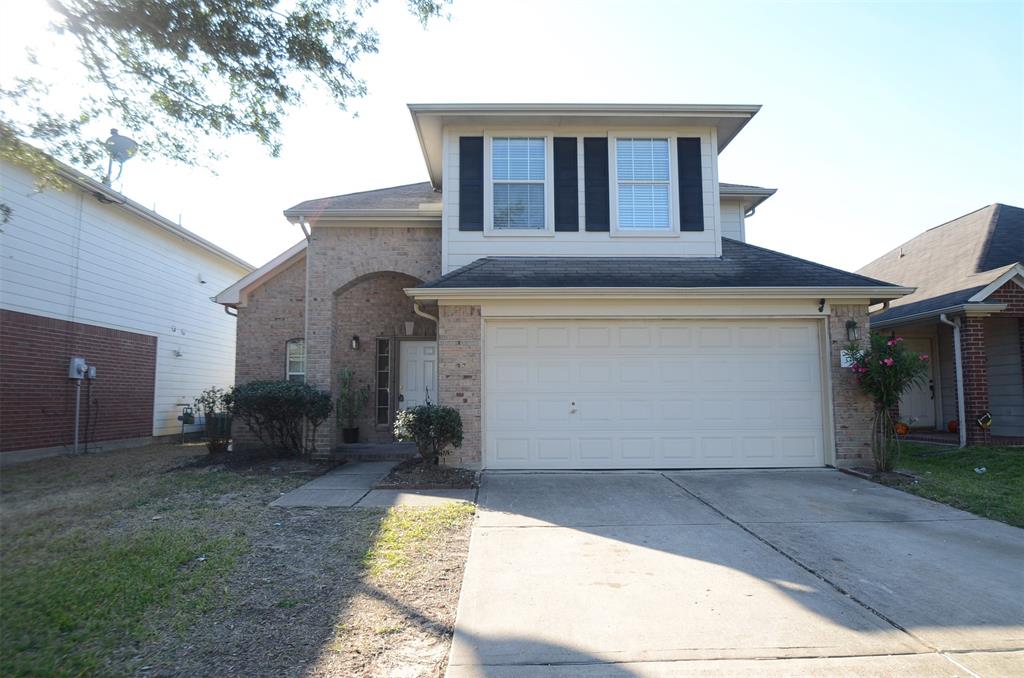 This is a two-story home featuring a brick facade with an arched entryway and a two-car garage. The house has a small front yard, and there's a notable second-floor window feature above the garage.