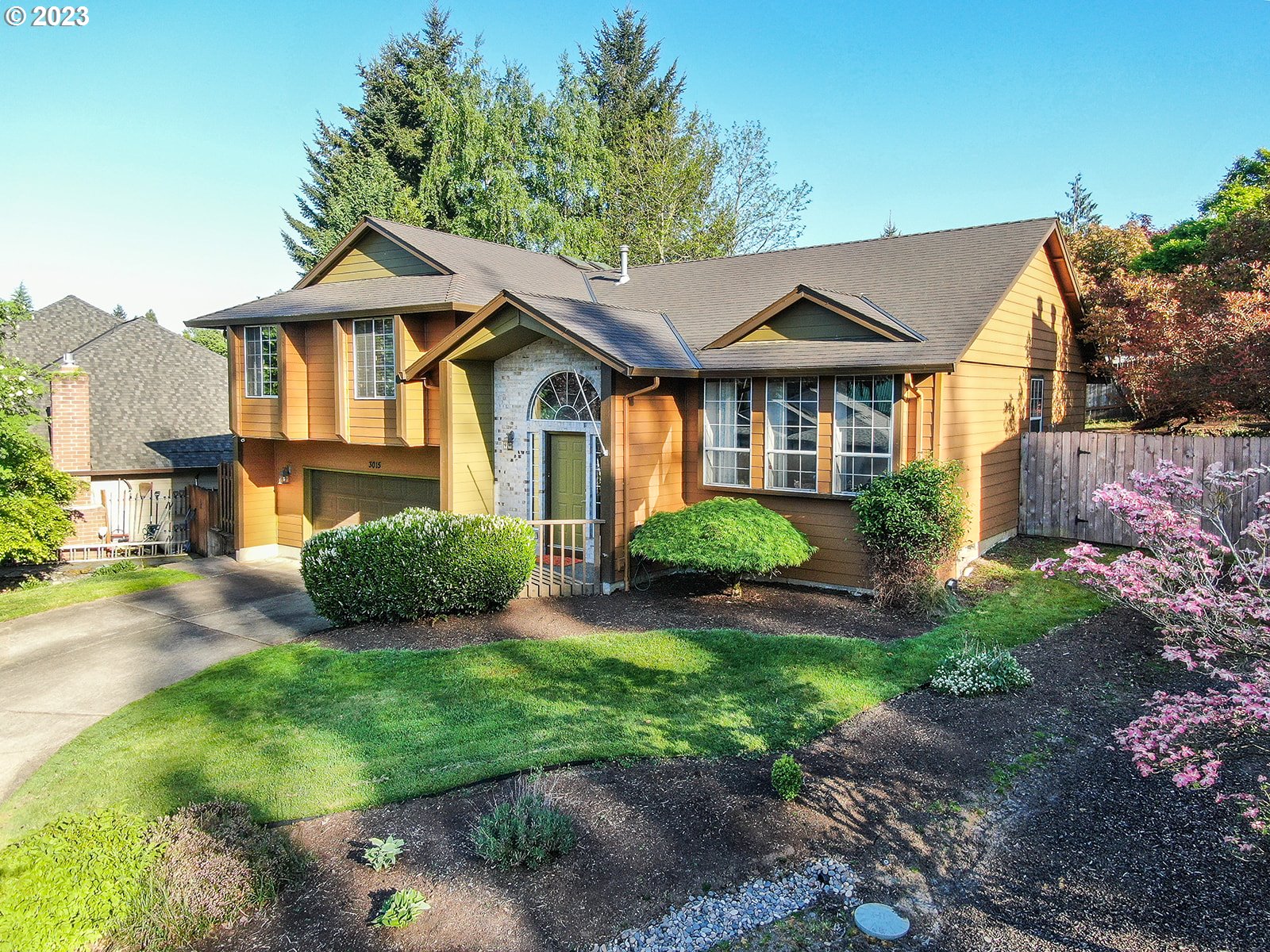 a view of a brick house with a yard plants and large tree