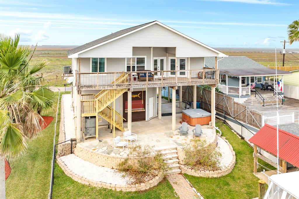 56 Marlin an elevated coastal home with a spacious deck and staircase access. Features a large patio area with seating, a hot tub, and landscaped surroundings. Ideal for enjoying outdoor and canal front living and scenic views.