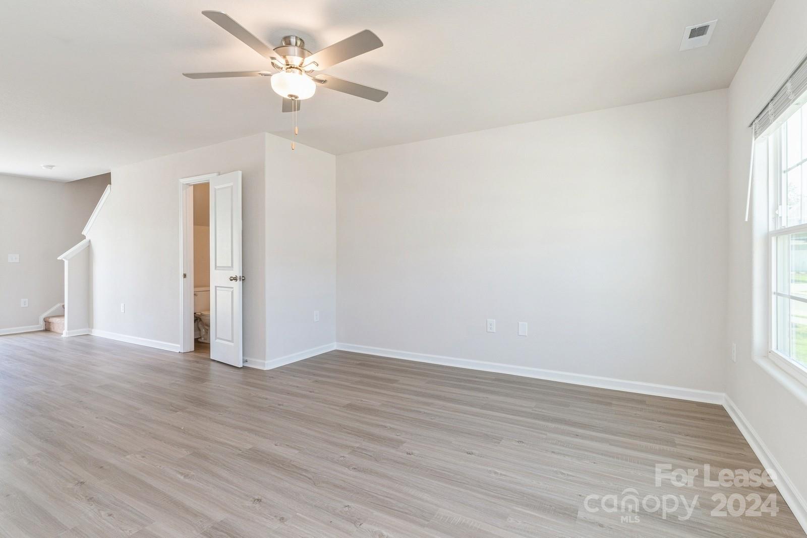 an empty room with wooden floor ceiling fan and windows