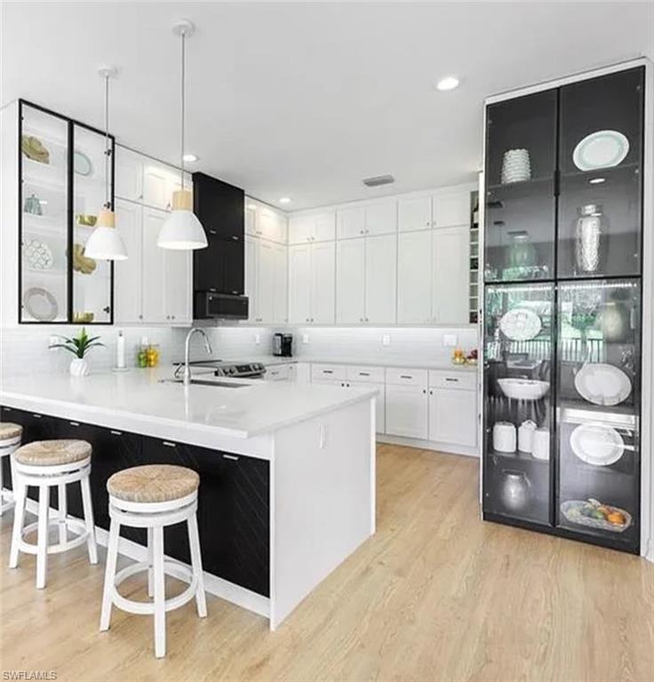 Kitchen featuring a kitchen bar, kitchen peninsula, white cabinetry, light hardwood / wood-style flooring, and decorative light fixtures