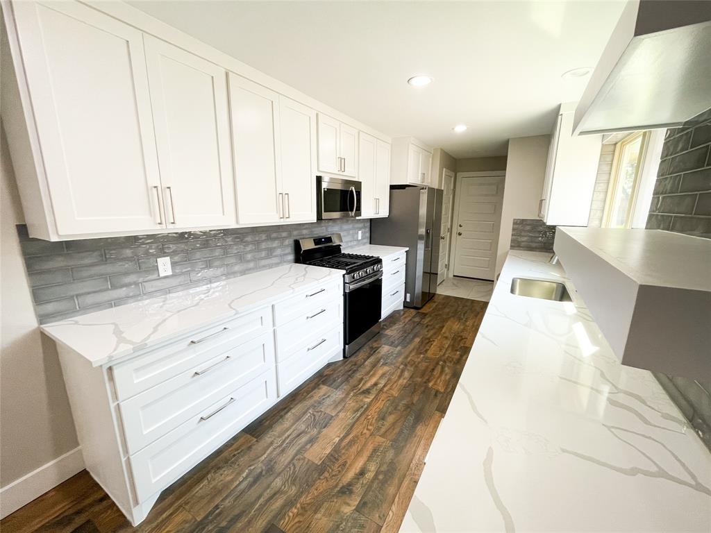 a large white kitchen with granite countertop a stove a sink a window and white cabinets