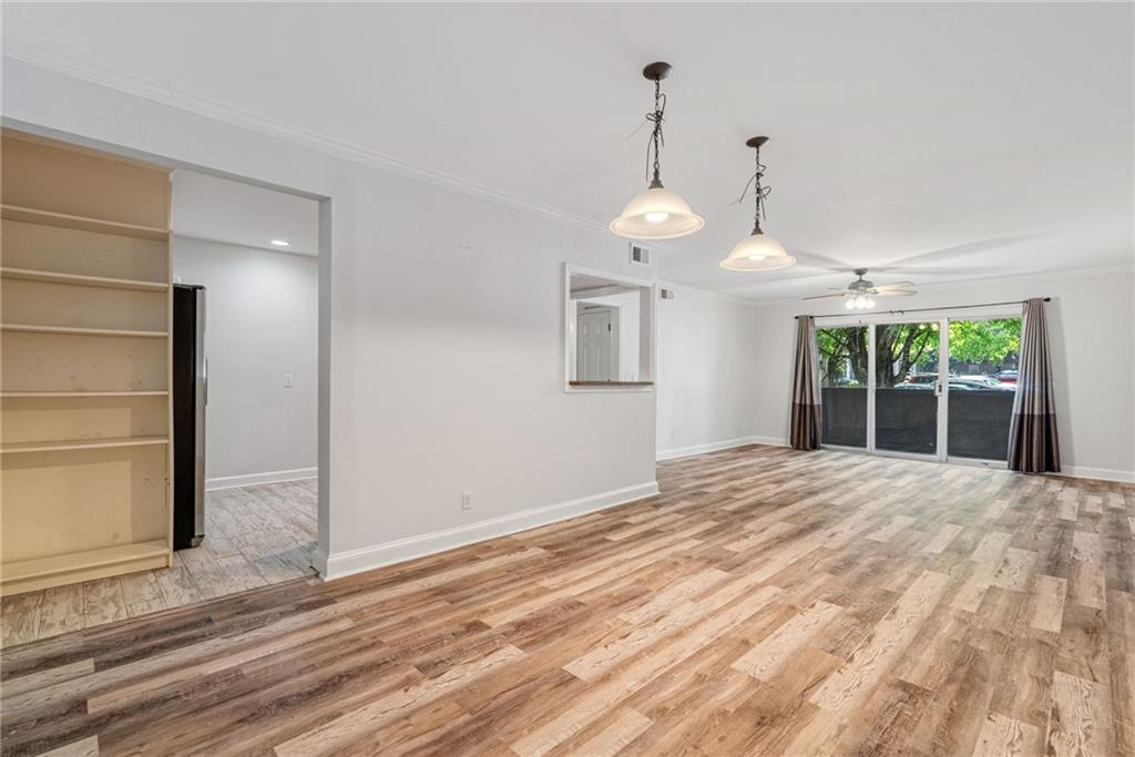 a view of an empty room with wooden floor kitchen view and a window