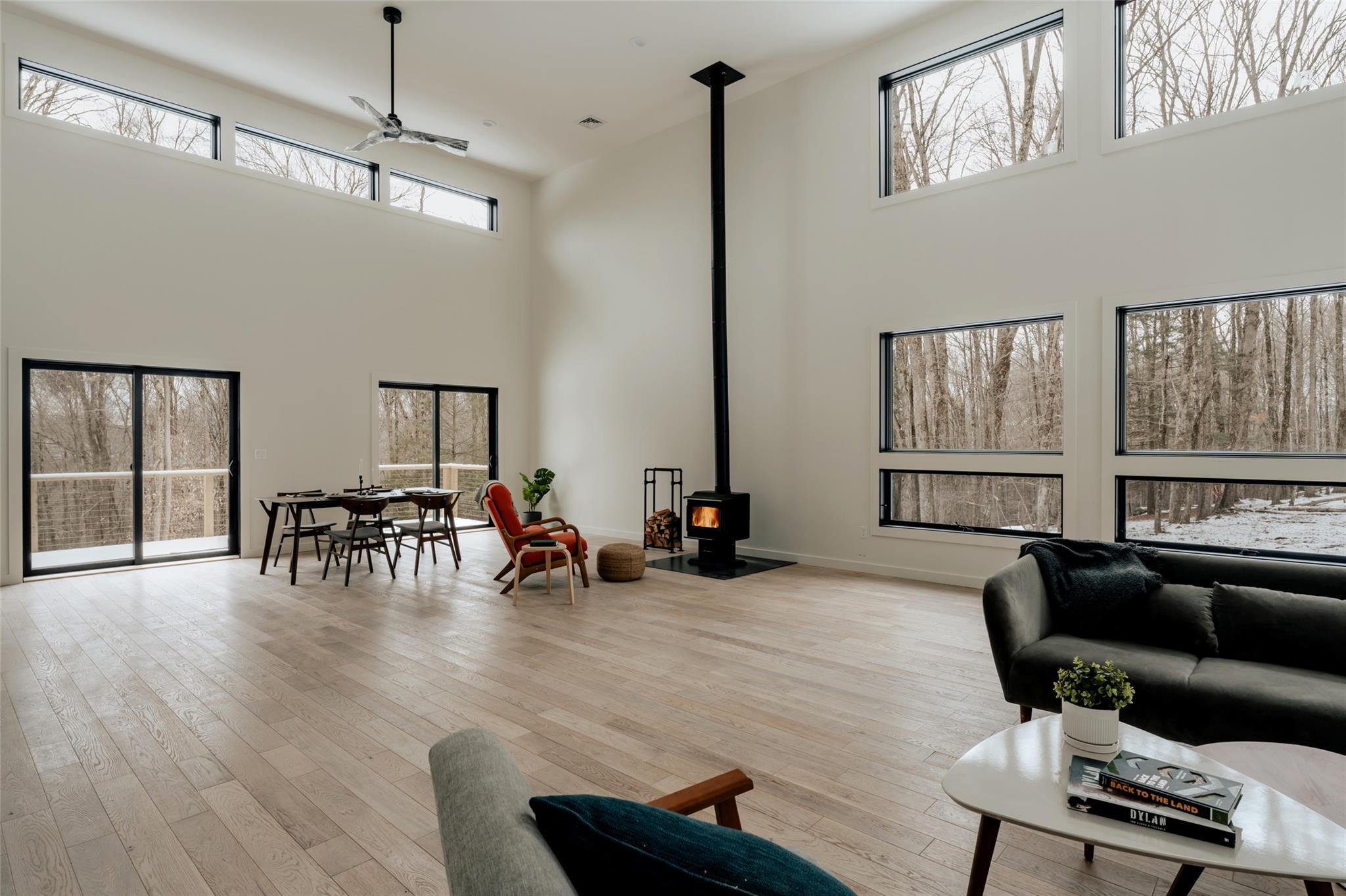 Living room featuring ceiling fan, light hardwood / wood-style floors, a wood stove, and a high ceiling