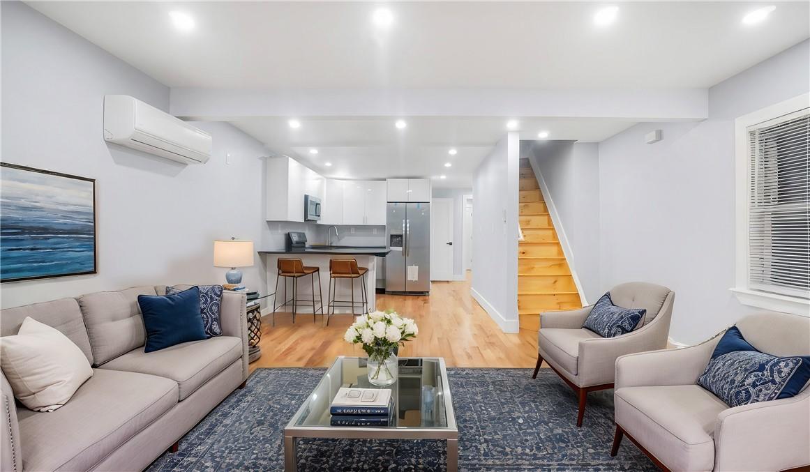 Living room with beamed ceiling, a wall mounted AC, and light hardwood / wood-style flooring