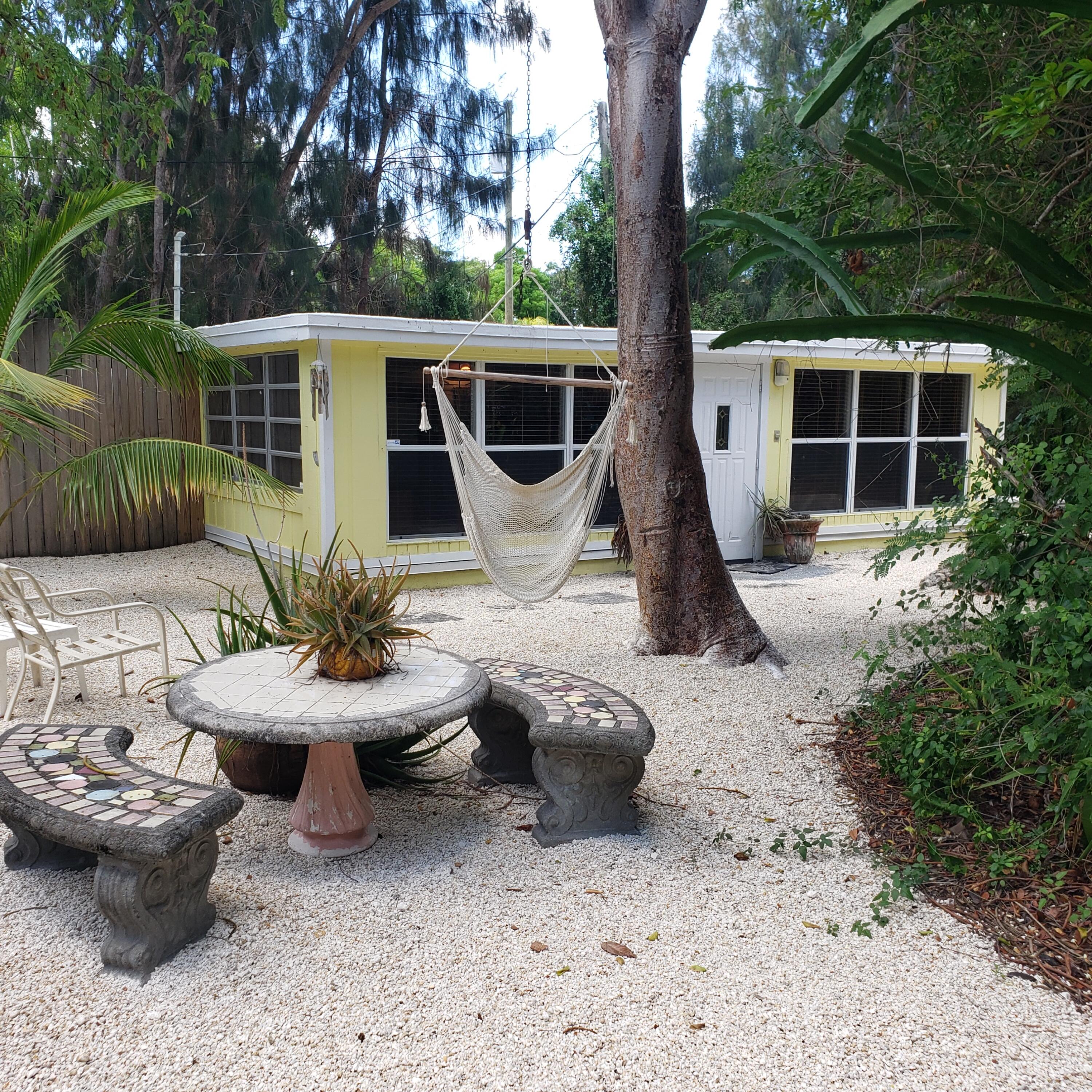 a view of a backyard with table and chairs potted plants and a large tree