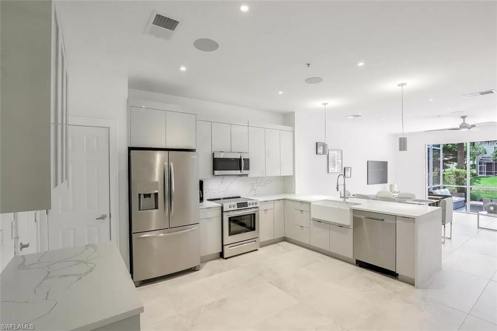 Kitchen with stainless steel appliances, sink, kitchen peninsula, light tile patterned flooring, and ceiling fan