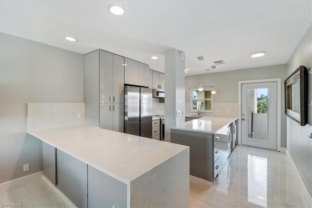 Kitchen featuring sink, hanging light fixtures, gray cabinets, stainless steel fridge, and kitchen peninsula