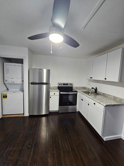 Kitchen featuring sink, dark hardwood / wood-style floors, appliances with stainless steel finishes, white cabinetry, and stacked washer / dryer