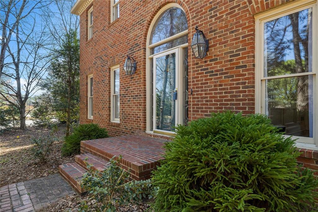 a view of a brick house with a yard plants and large tree