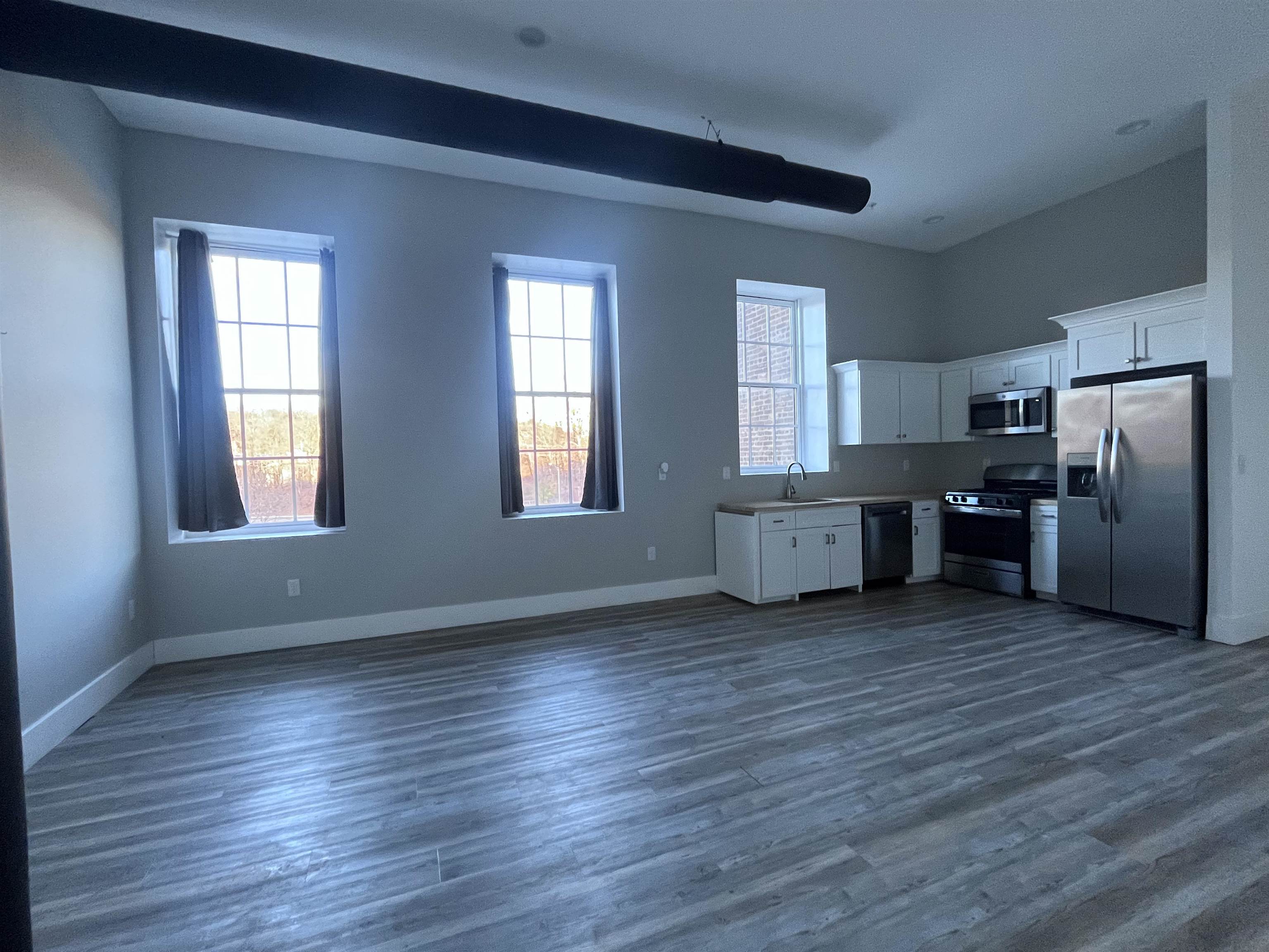 a view of a kitchen with wooden floor electronic appliances and windows