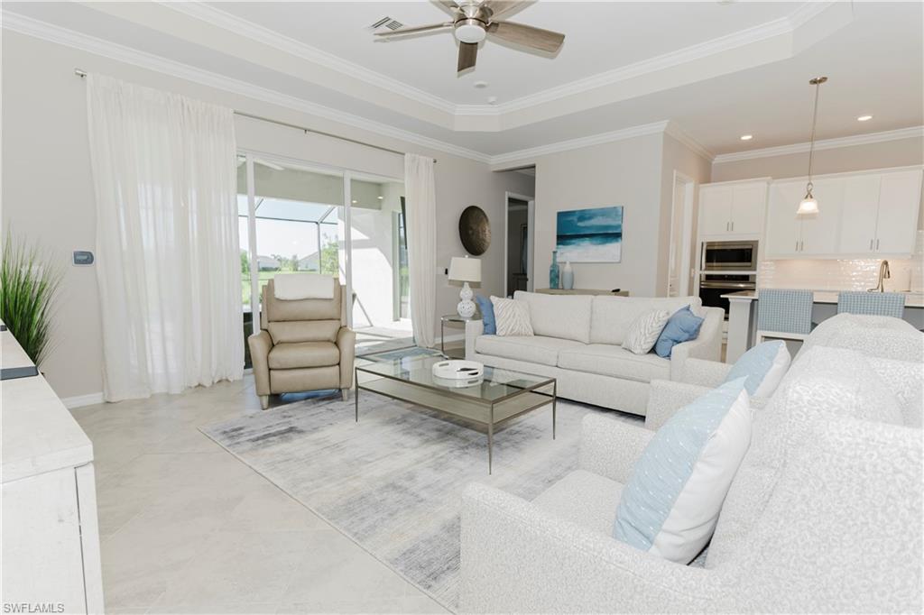 Living room featuring light tile patterned floors, a raised ceiling, ceiling fan, and ornamental molding