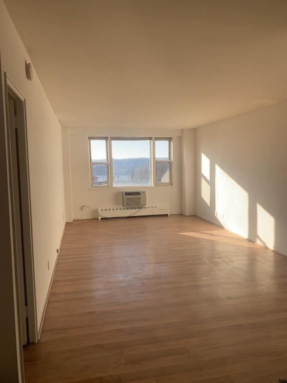 Empty room with wood-type flooring, baseboard heating, and a wall unit AC