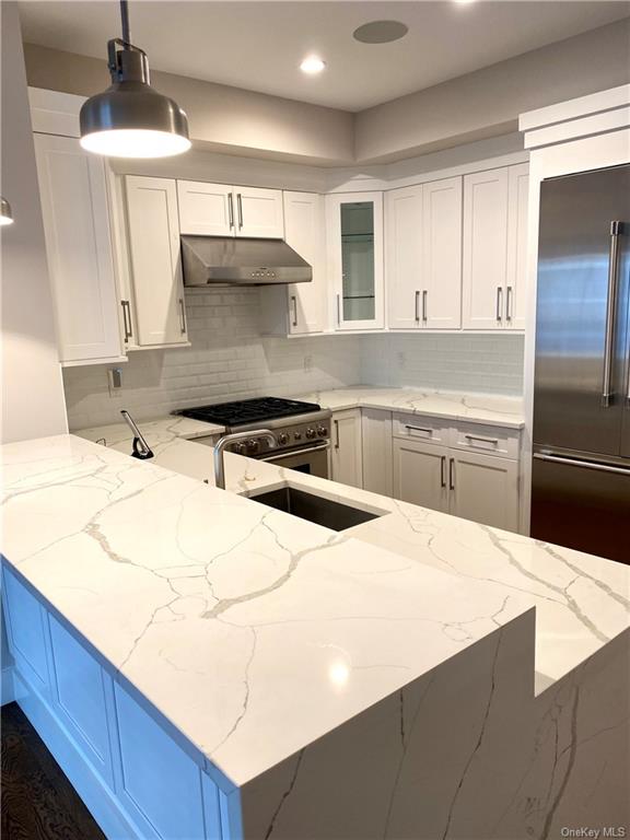 Kitchen with high end appliances, light stone countertops, decorative light fixtures, white cabinetry, and tasteful backsplash