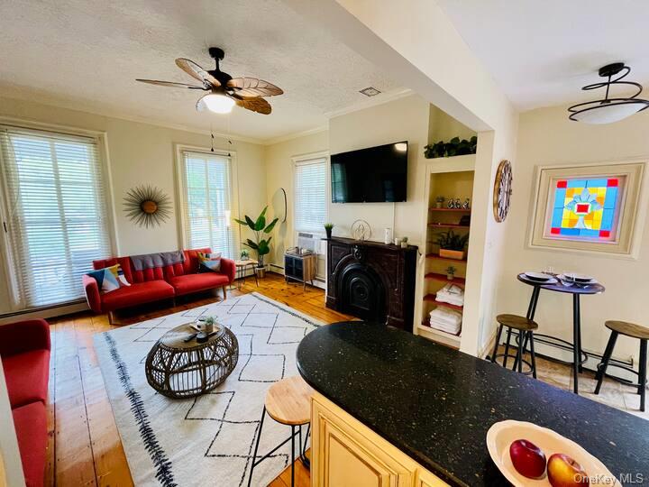 Living room with ceiling fan, a textured ceiling, light hardwood / wood-style flooring, ornamental molding, and baseboard heating