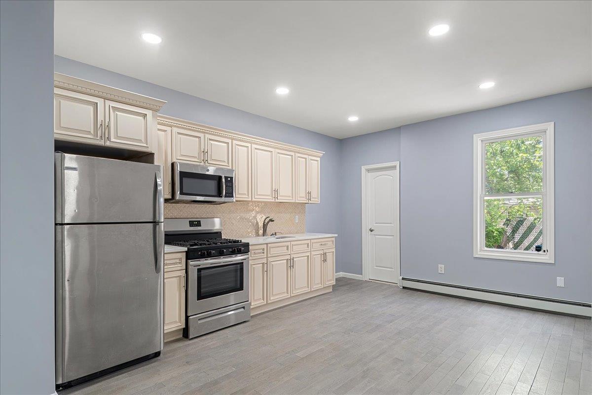 Kitchen featuring cream cabinetry, baseboard heating, and appliances with stainless steel finishes