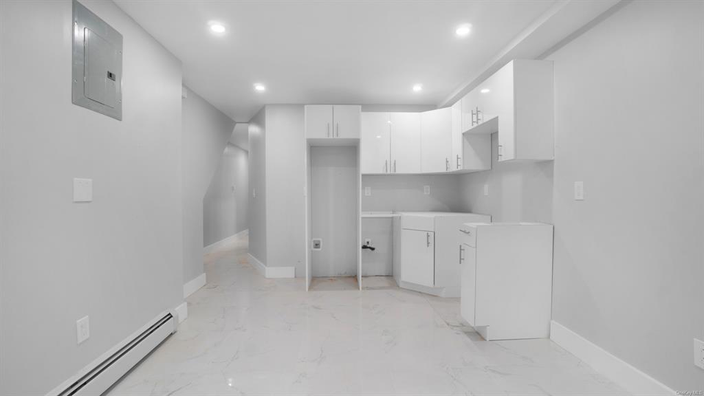 Kitchen with electric panel, a baseboard radiator, and white cabinets