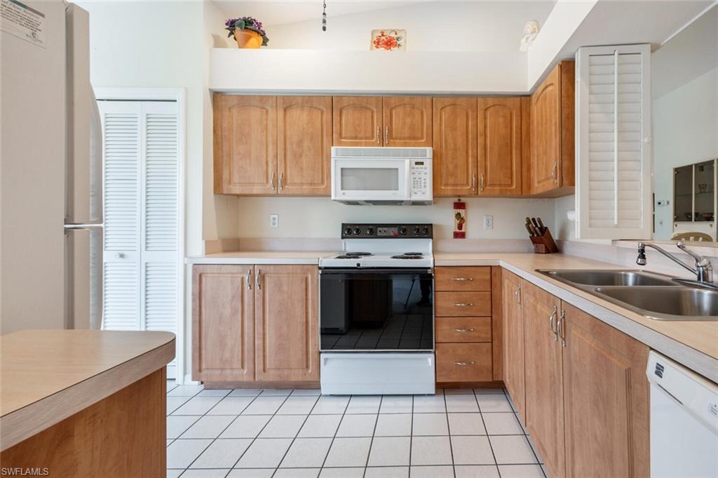 Kitchen with light tile patterned floors, white appliances, vaulted ceiling, and sink