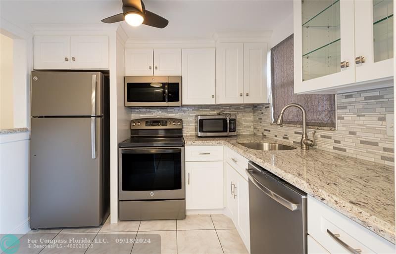 a kitchen with granite countertop a sink stainless steel appliances and white cabinets