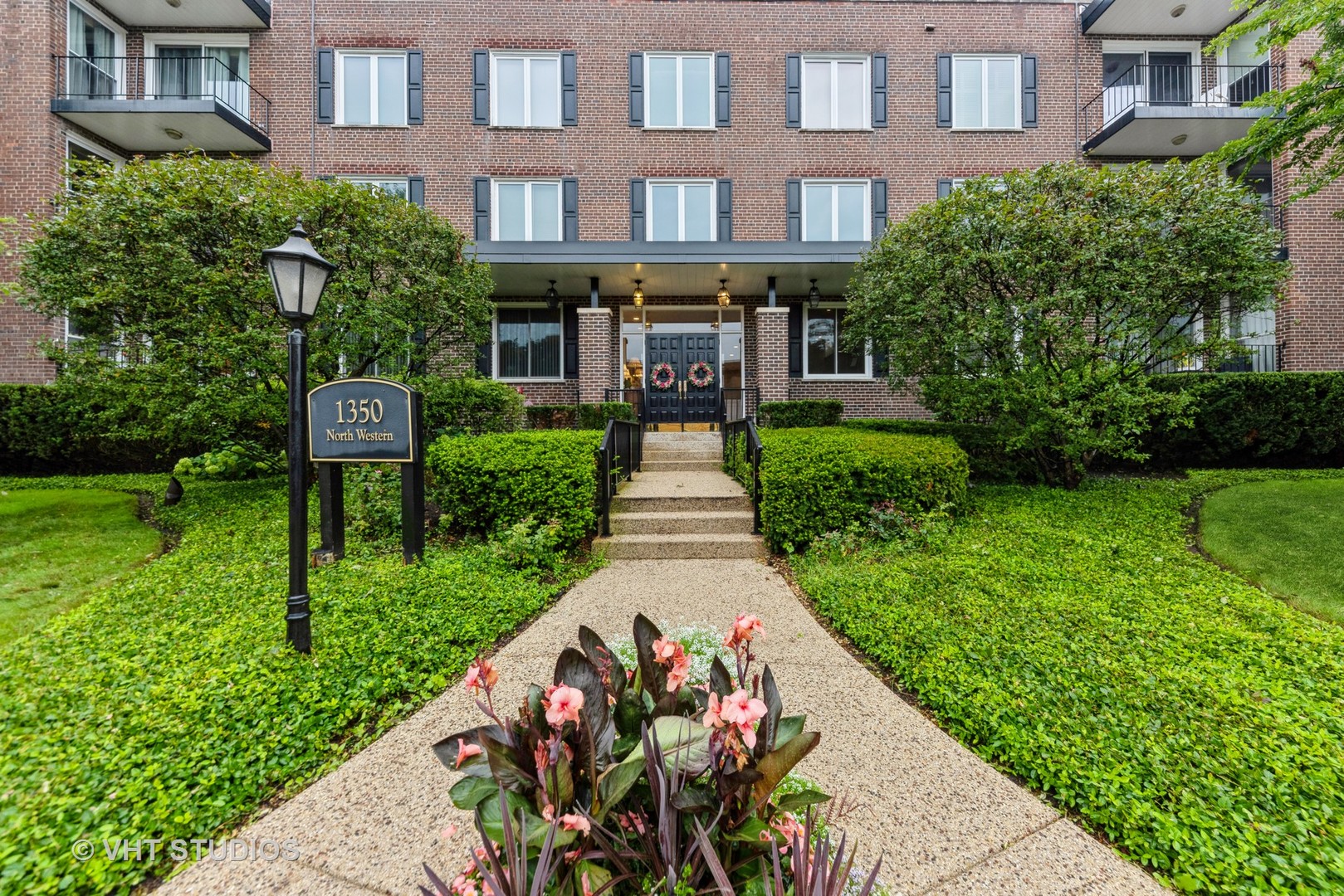 a front view of a multi story residential apartment building with a yard and potted plants