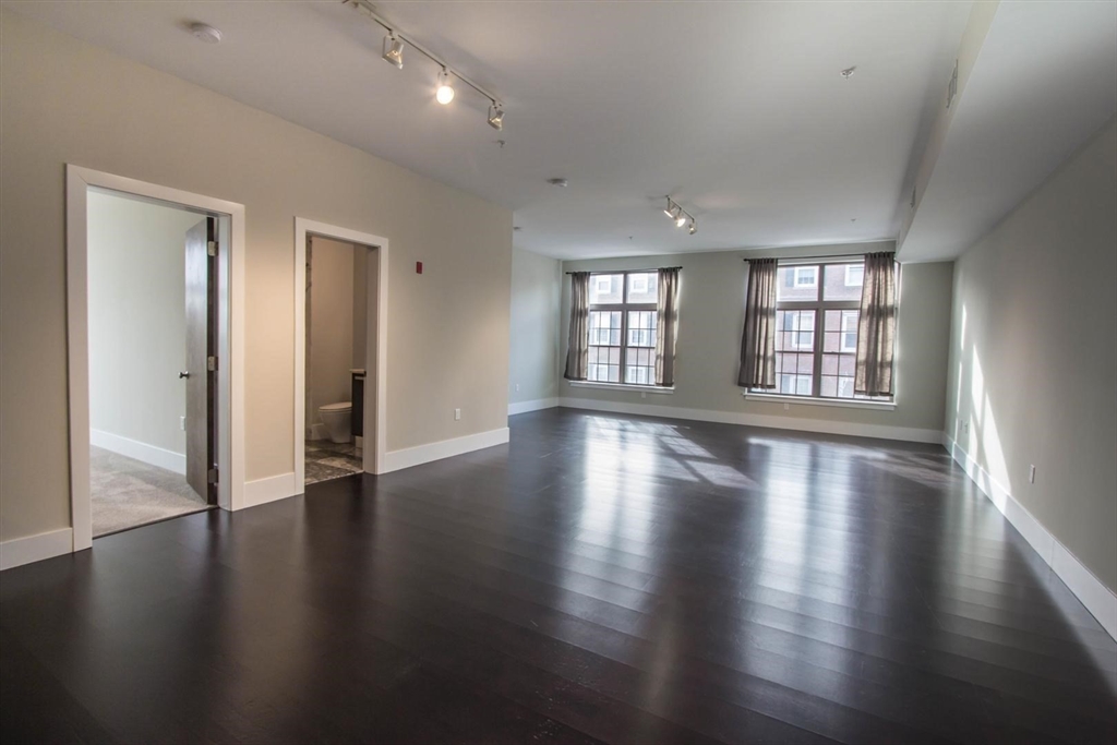 an empty room with wooden floor and windows with curtains