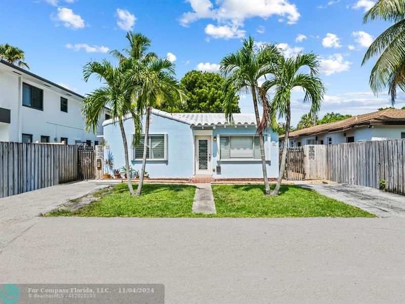 a palm tree sitting in front of a house with wooden fence