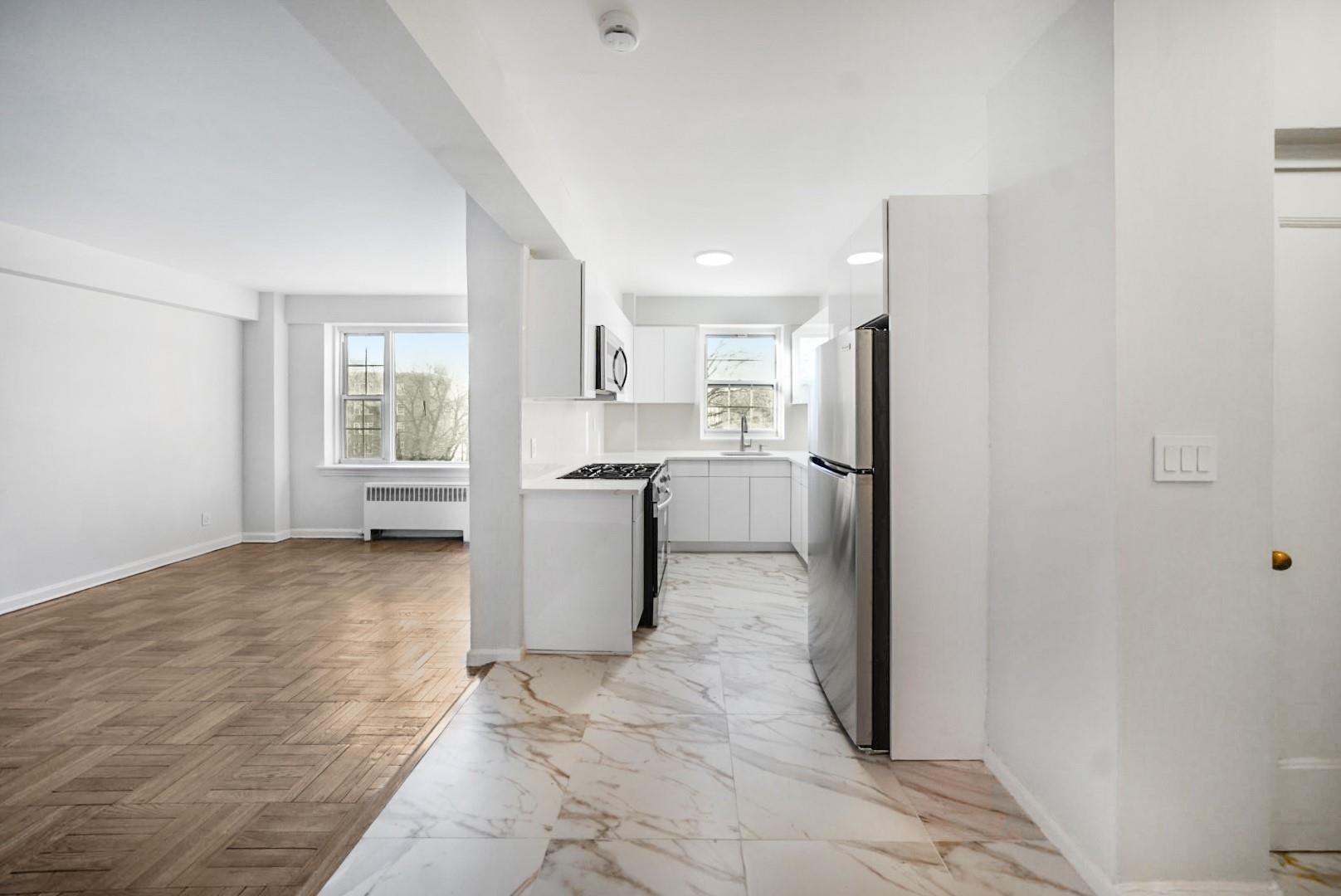 Kitchen with light parquet floors, sink, radiator heating unit, white cabinetry, and stainless steel appliances