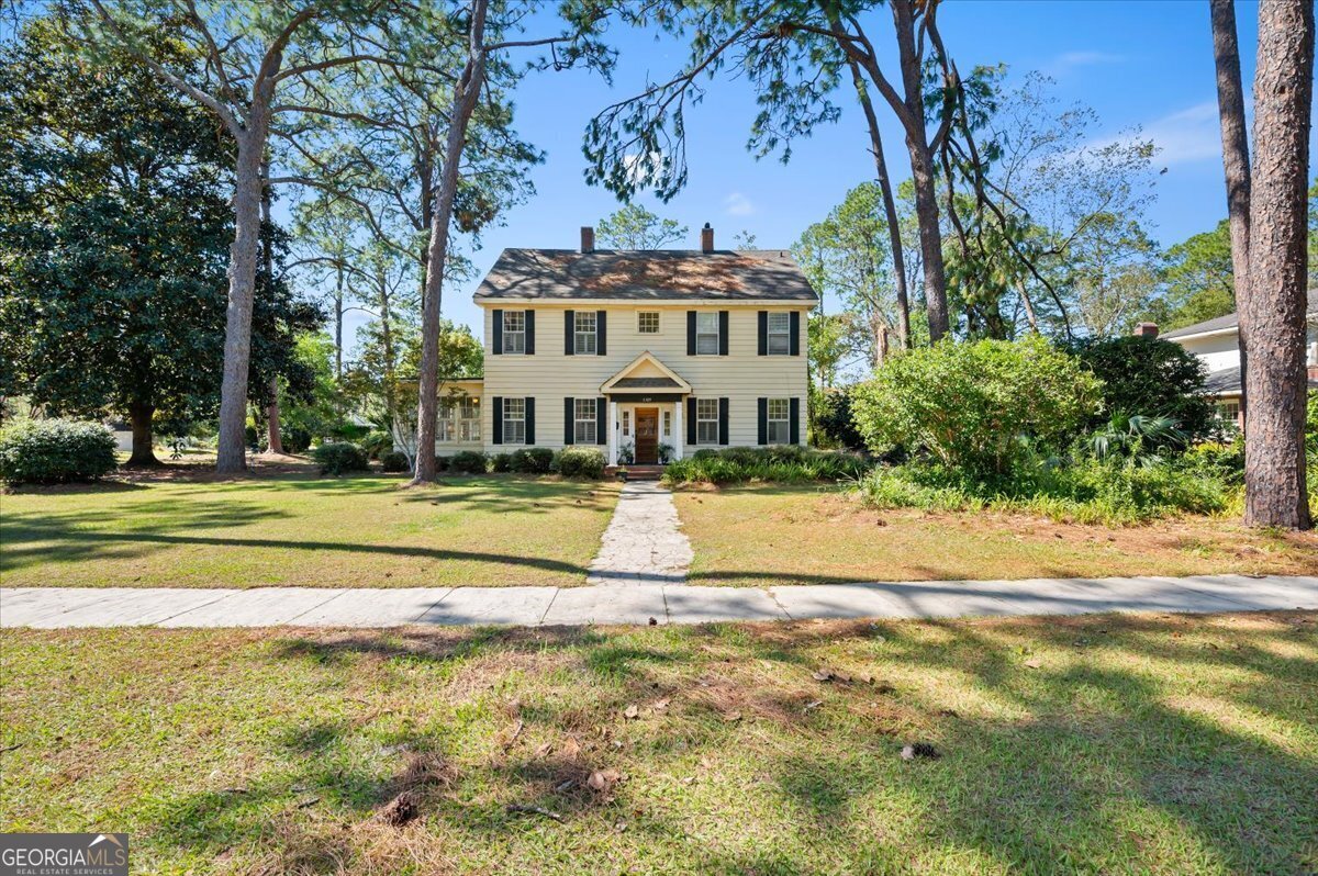 a view of a white house with a large pool and a yard with plants and large trees