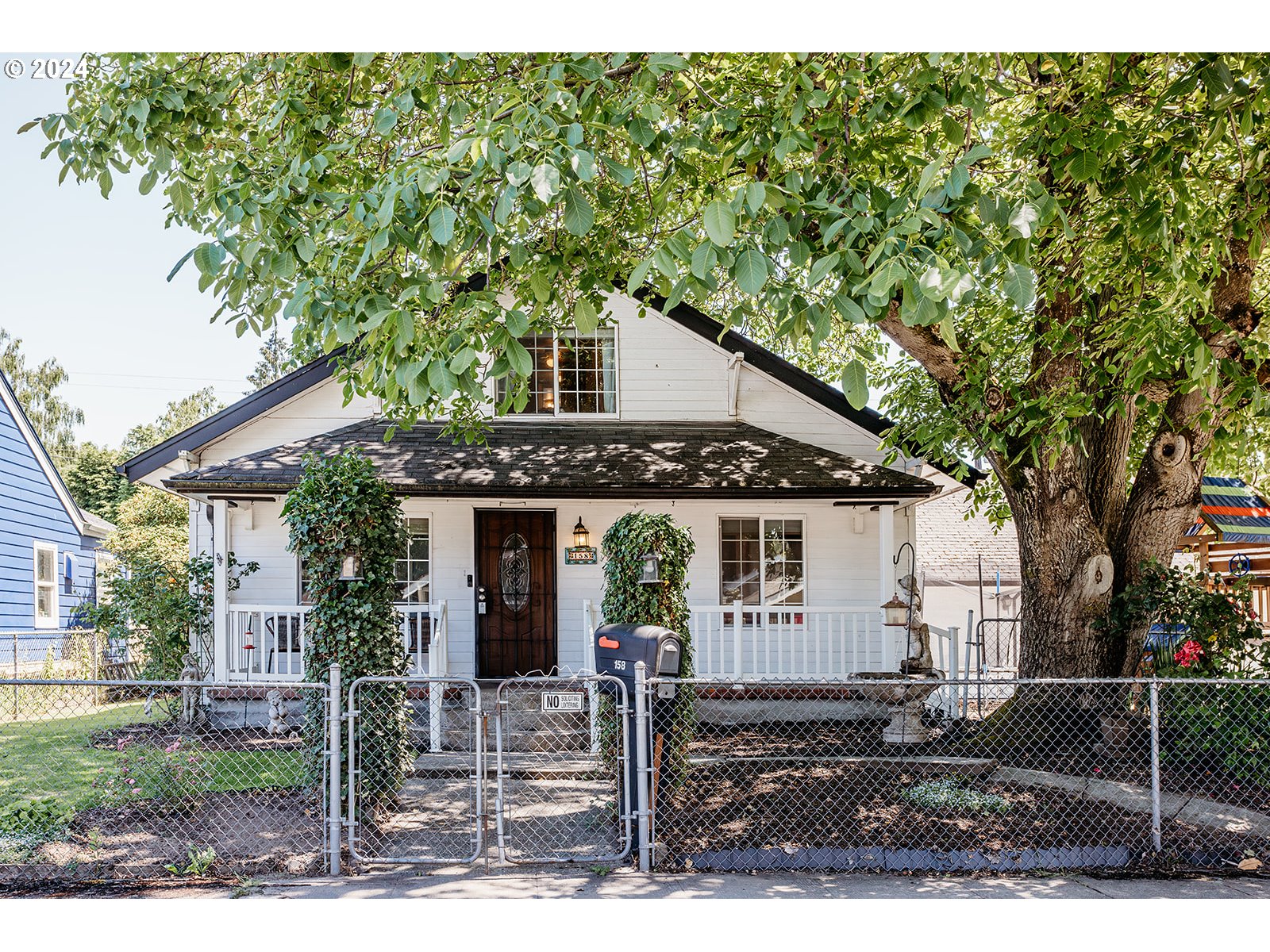 a view of a white house with a tree and wooden fence