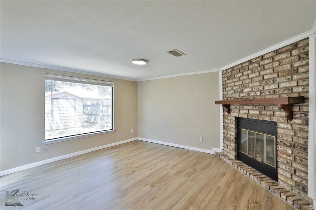 a view of an empty room with wooden floor fireplace and a window