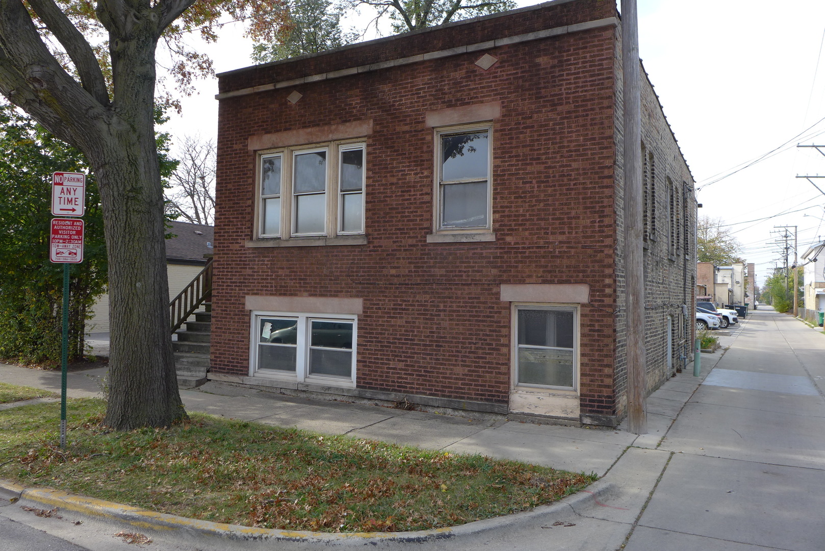 a view of a brick house with a small yard plants and a large tree