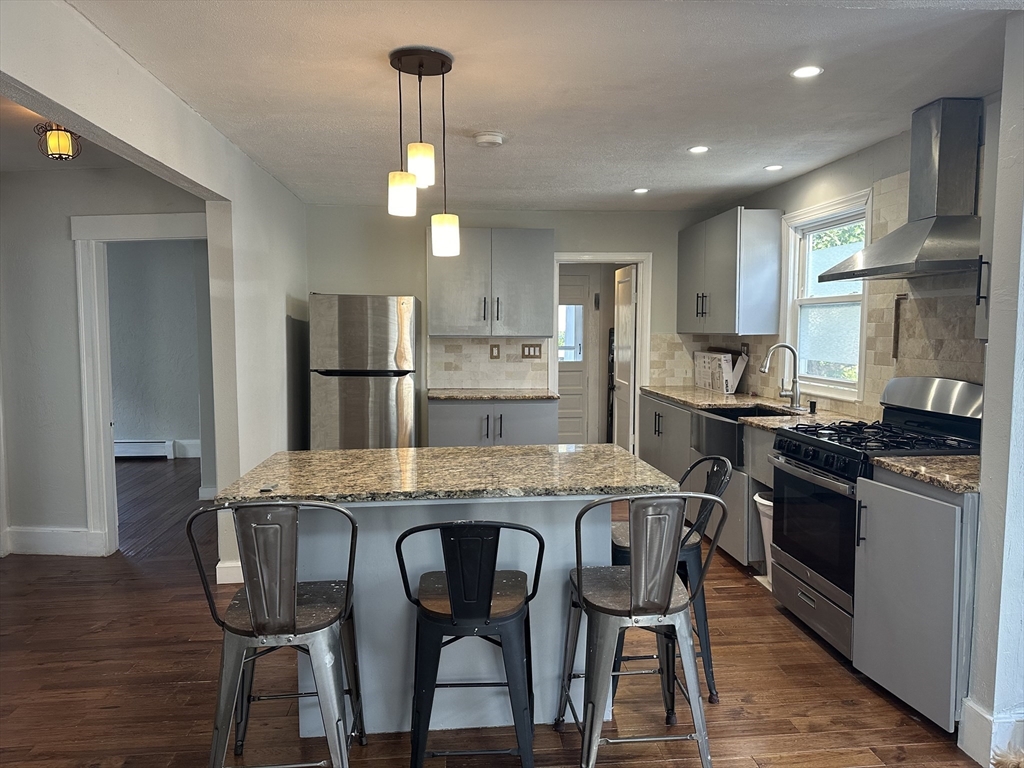 a kitchen with stainless steel appliances granite countertop a stove a refrigerator a kitchen island a dining table and chairs with wooden floor