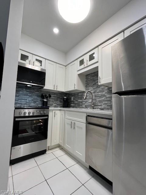 Kitchen featuring light tile patterned flooring, white cabinetry, appliances with stainless steel finishes, and tasteful backsplash