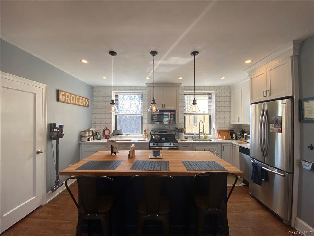 Kitchen with dark wood-type flooring, stainless steel appliances, a center island, white cabinets, and tasteful backsplash