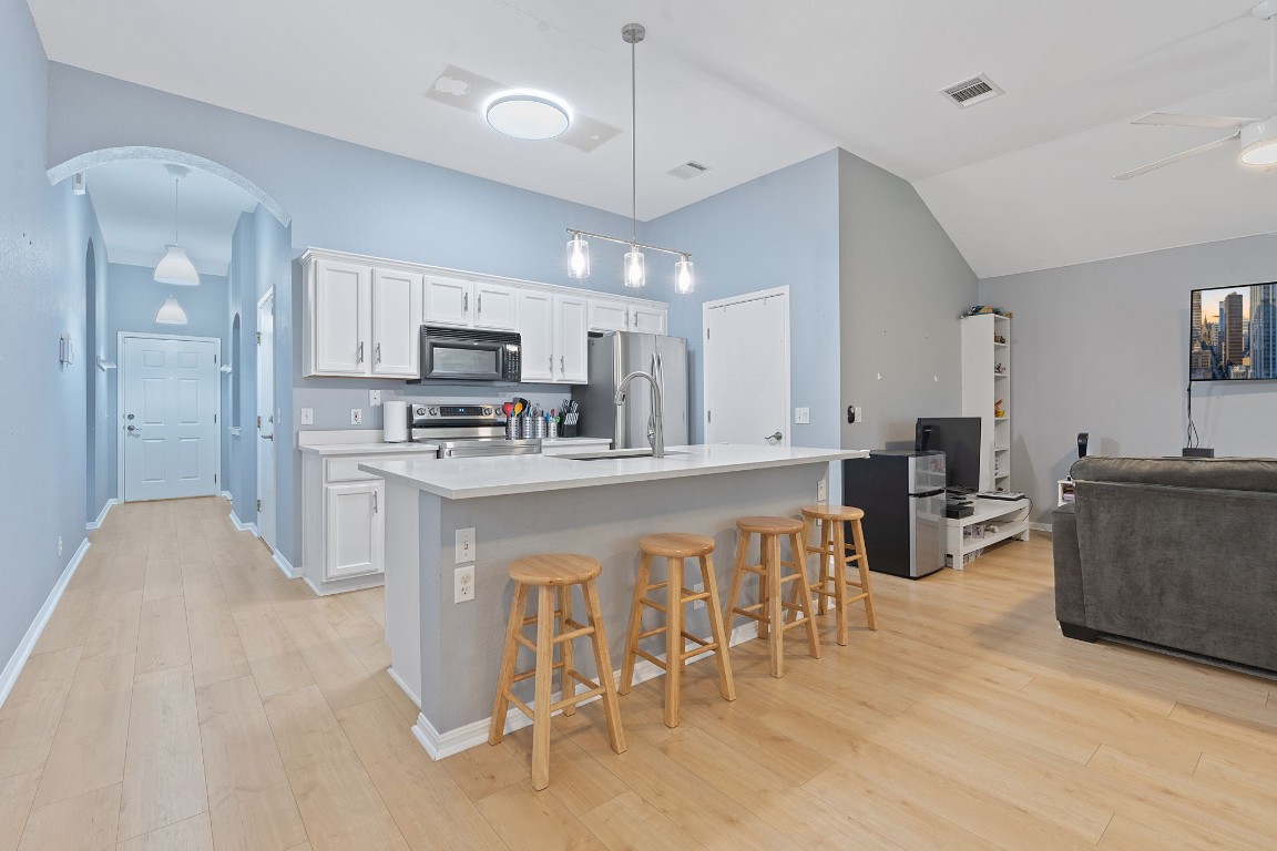 a kitchen with stainless steel appliances kitchen island granite countertop a stove a sink a refrigerator a dining table and chairs with wooden floor