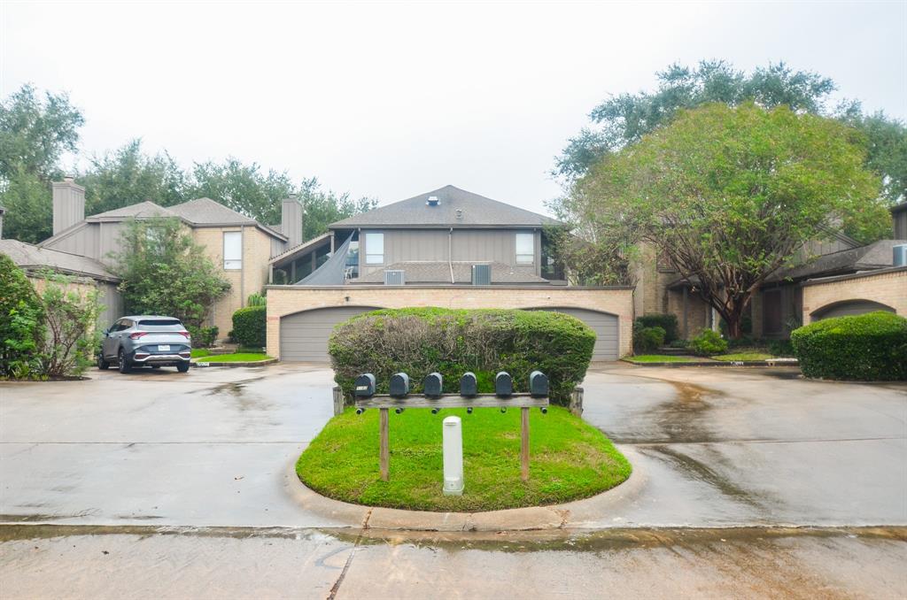 This is a two-story brick home featuring a two-car garage, a well-maintained lawn with mature landscaping, and a shaded driveway. The residence has a prominent upper-level balcony and a traditional architectural style.