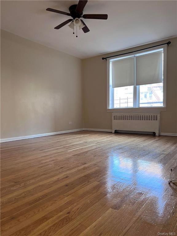 Unfurnished room featuring radiator heating unit, ceiling fan, and hardwood / wood-style floors