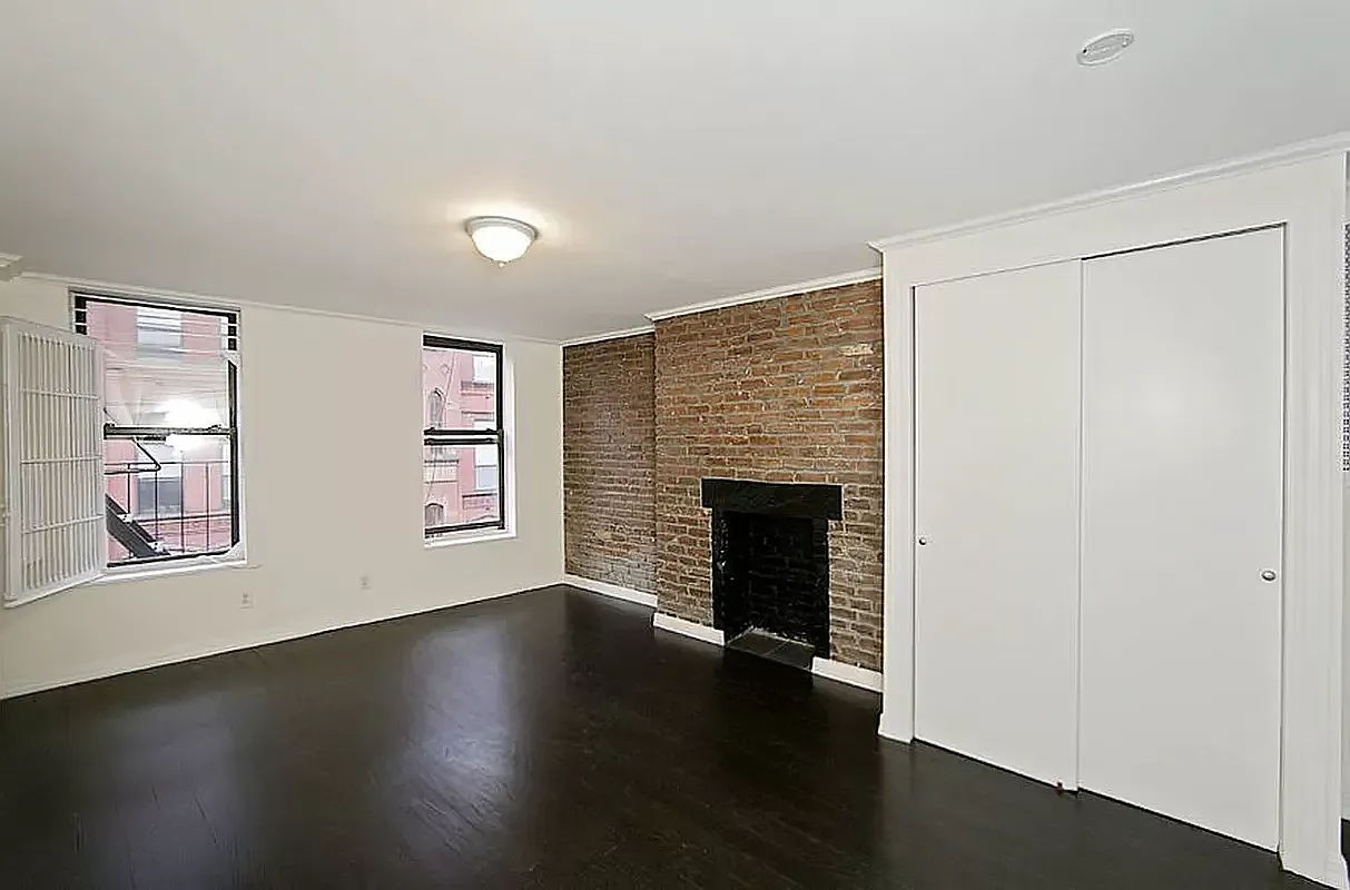 an empty room with wooden floor fireplace and windows