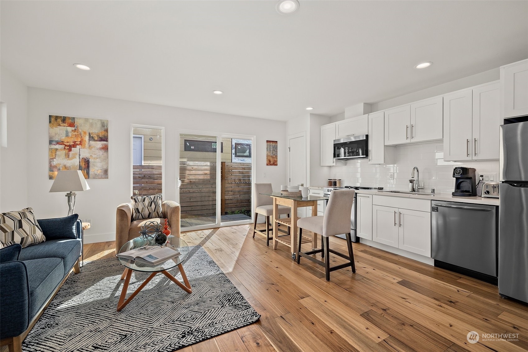 a living room with furniture a dining table wooden floor and kitchen view