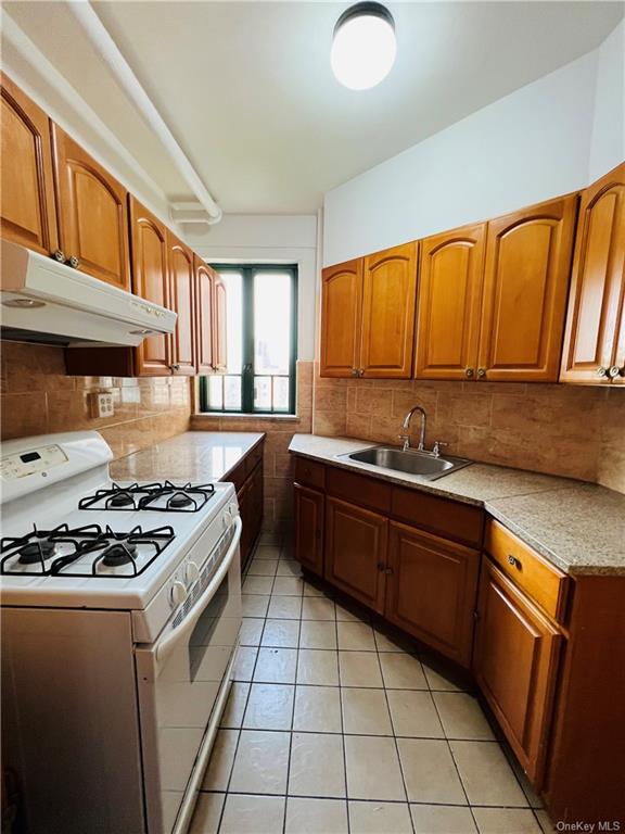 Kitchen with sink, white gas range oven, backsplash, and light tile floors