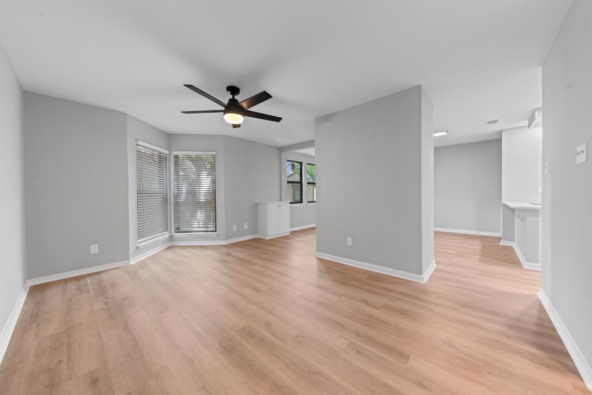 a view of an empty room with wooden floor and a ceiling fan