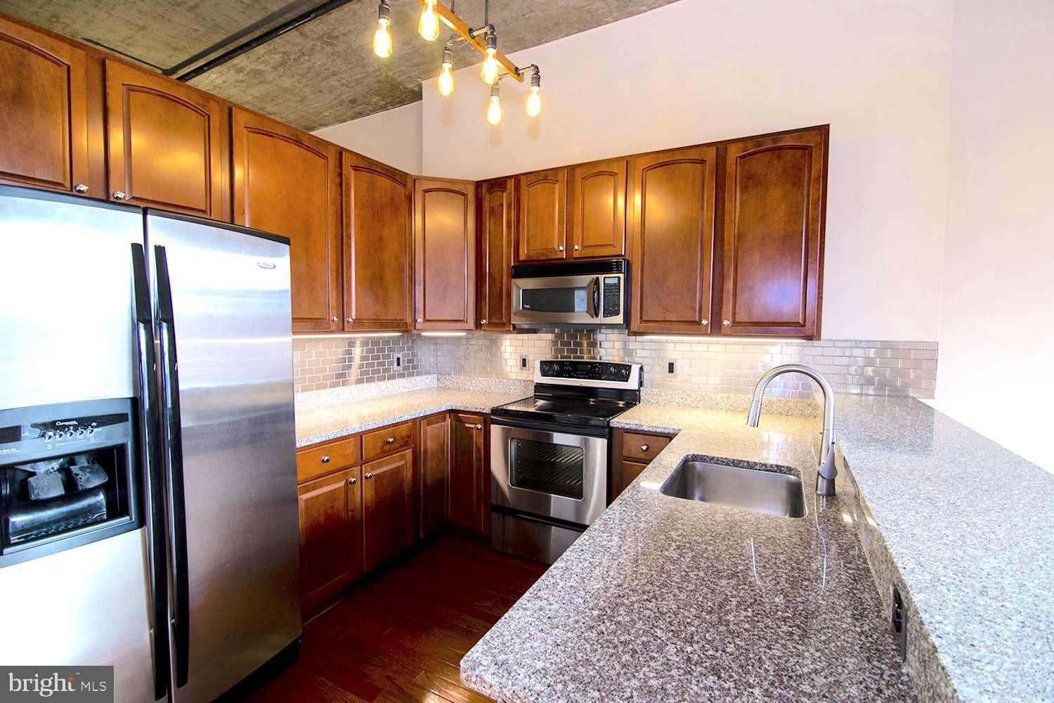 a kitchen with granite countertop wooden cabinets a refrigerator stove top oven and sink