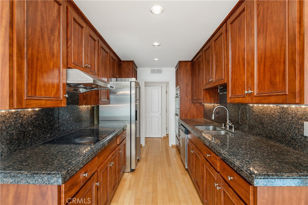 a kitchen with stainless steel appliances granite countertop a sink a stove and a wooden cabinets