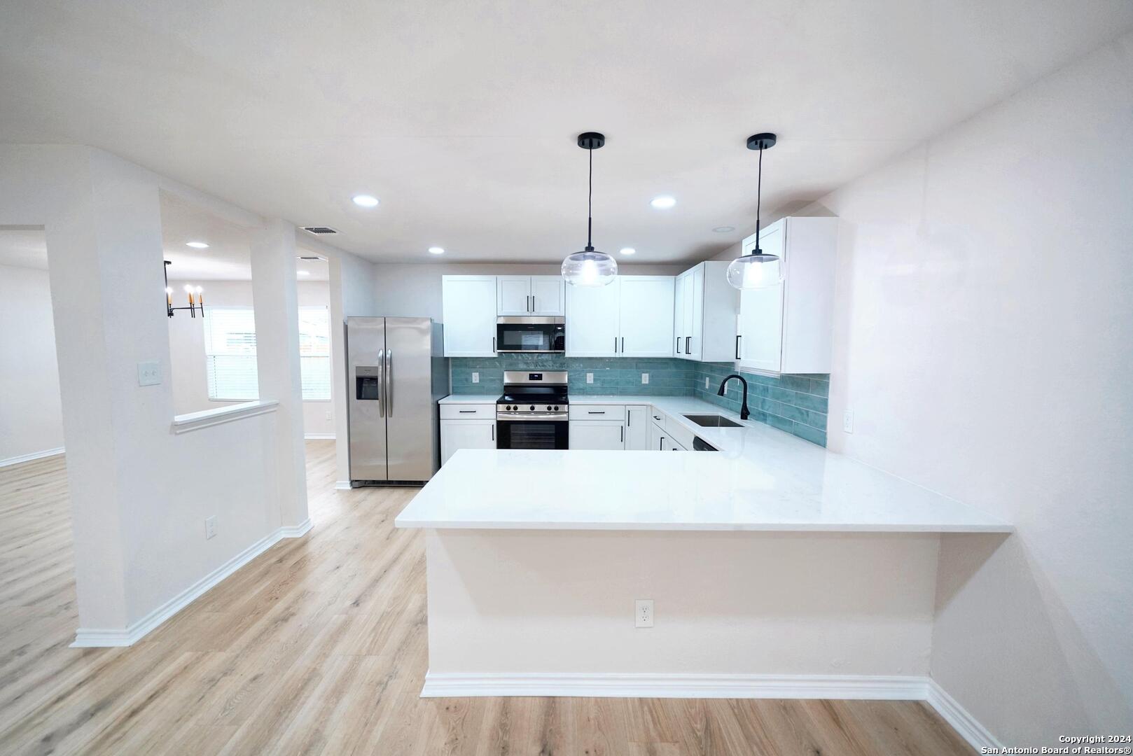 a large white kitchen with kitchen island a sink stainless steel appliances and cabinets