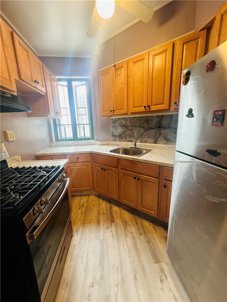 Kitchen featuring backsplash, light hardwood / wood-style floors, stainless steel appliances, sink, and ceiling fan