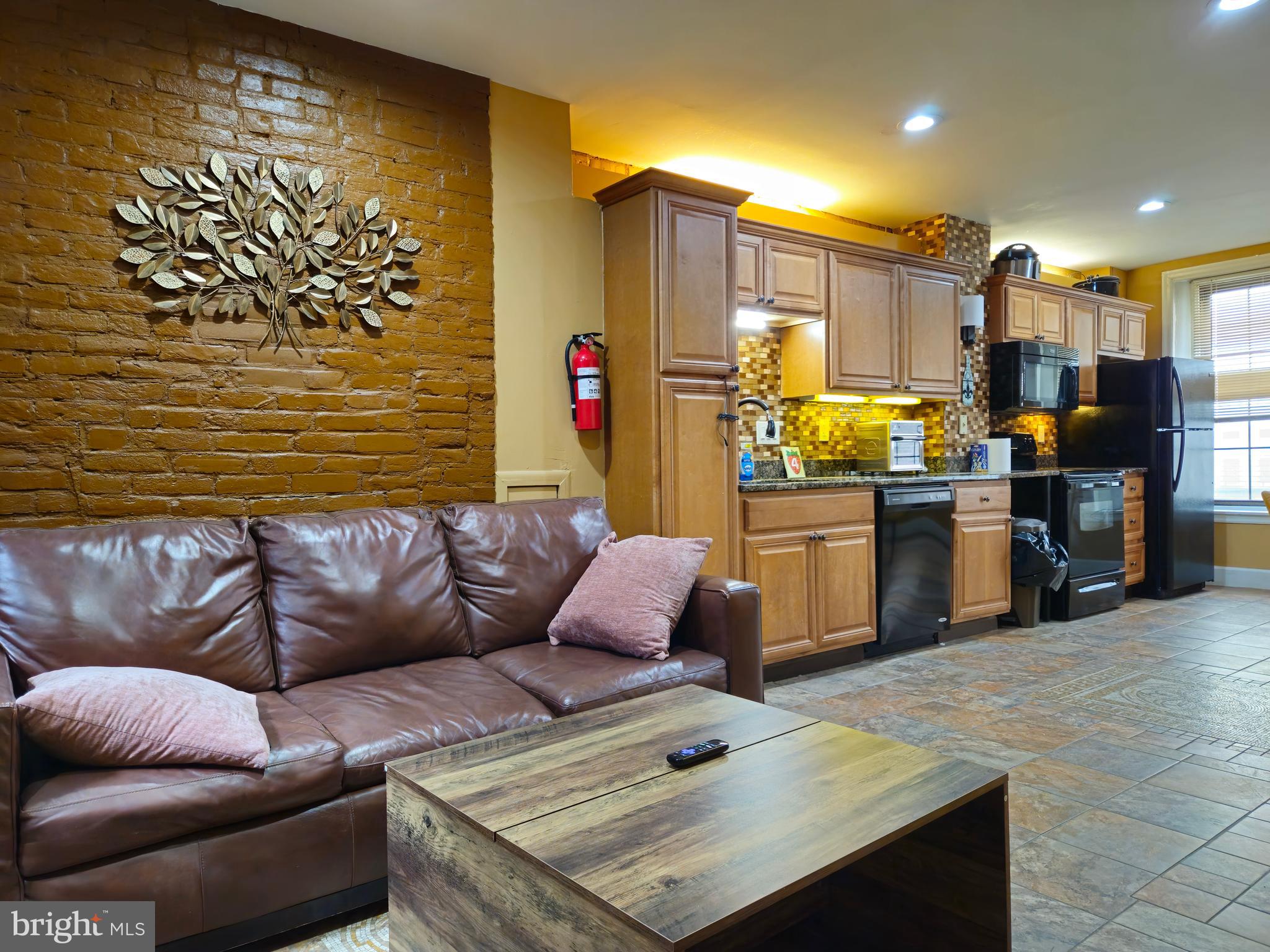 a living room with stainless steel appliances furniture a rug and a kitchen