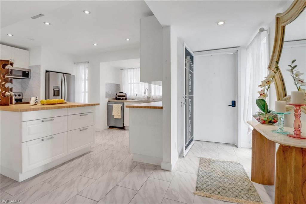 Kitchen featuring light tile patterned flooring, white cabinets, appliances with stainless steel finishes, butcher block countertops, and sink