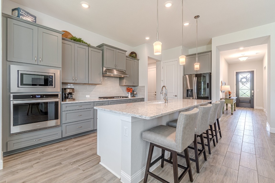 a large kitchen with stainless steel appliances kitchen island granite countertop a stove a sink a refrigerator and white cabinets with wooden floor