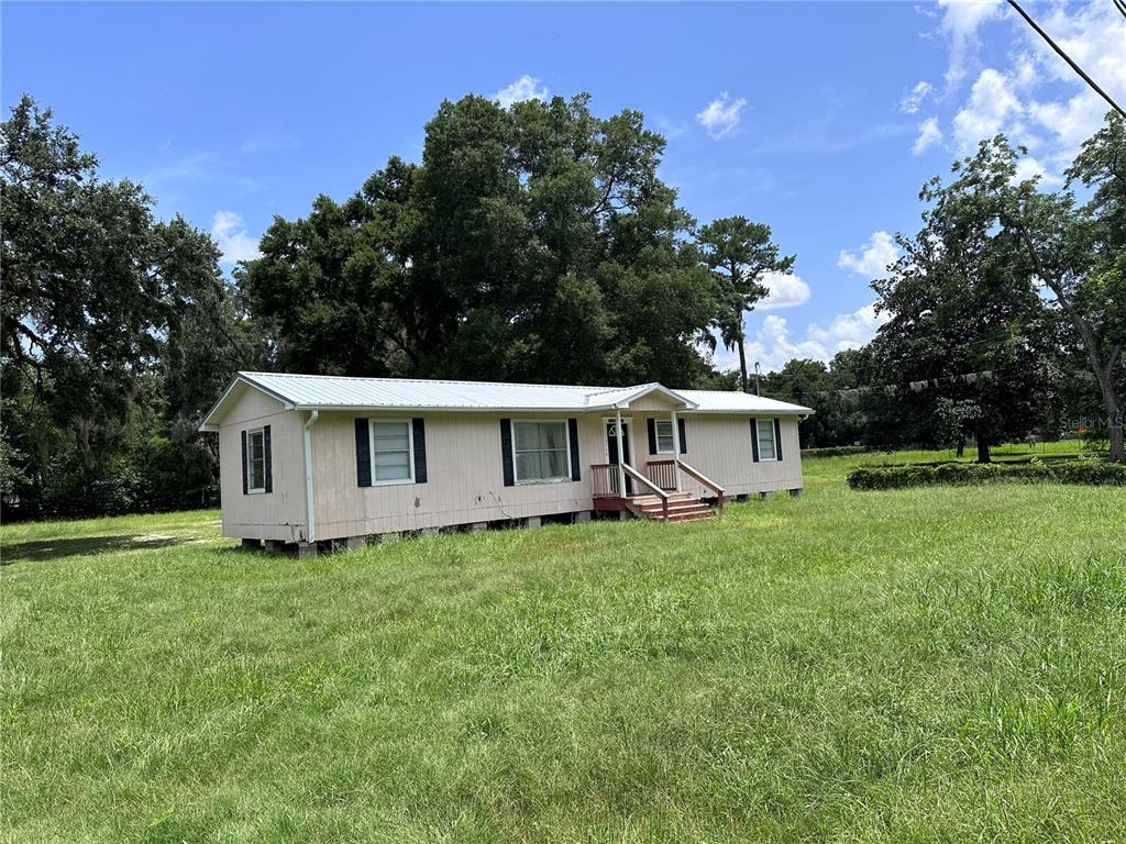 a house that is sitting in the grass with large trees and plants